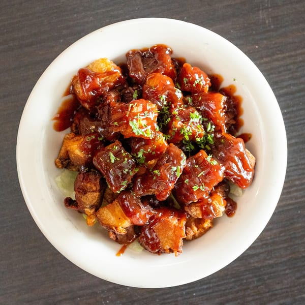 Crispy pork belly bites coated in a rich BBQ sauce and garnished with fresh parsley in a white bowl.