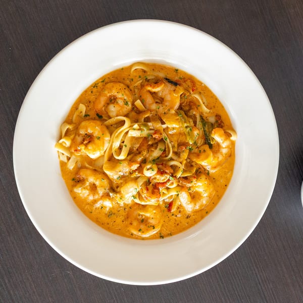 Creamy shrimp pasta with fettuccine noodles, red sauce, and green herbs in a white bowl.