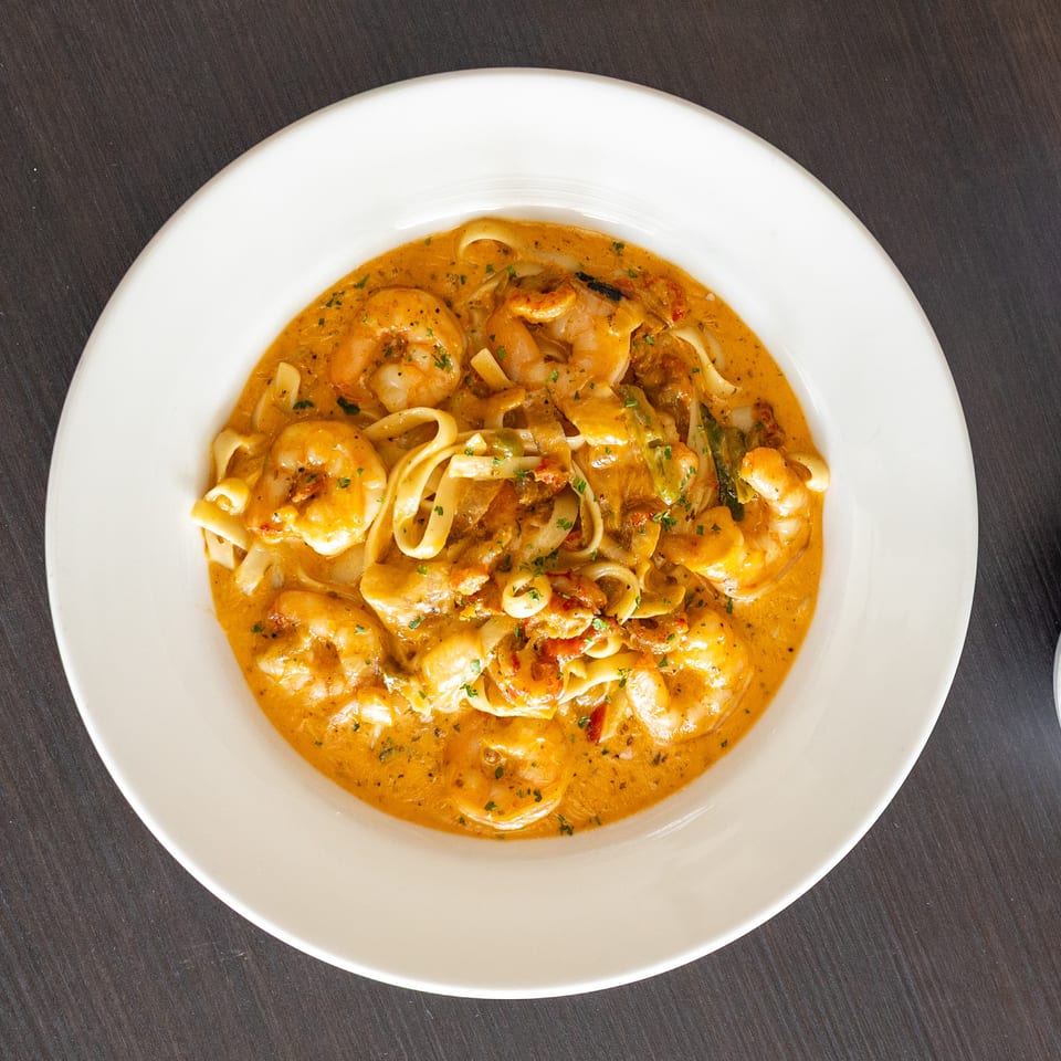 Creamy shrimp pasta with fettuccine noodles, red sauce, and green herbs in a white bowl.