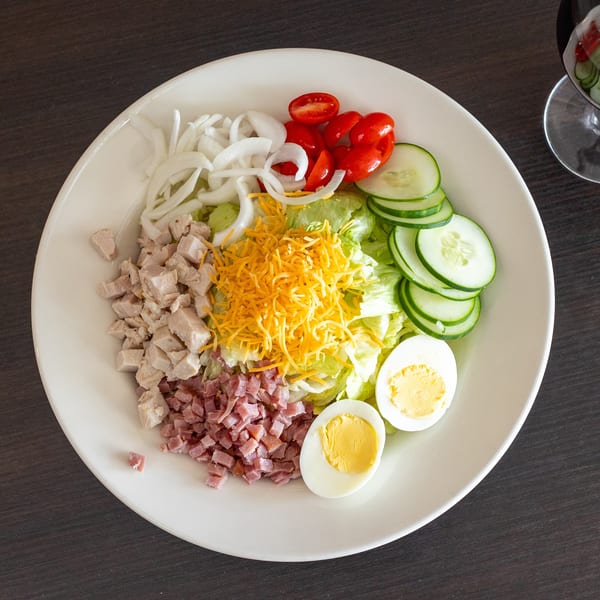Overhead view of a chef salad with chicken, ham, cheese, egg, and vegetables.