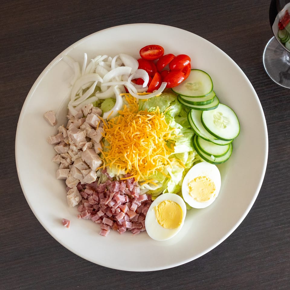 Overhead view of a chef salad with chicken, ham, cheese, egg, and vegetables.